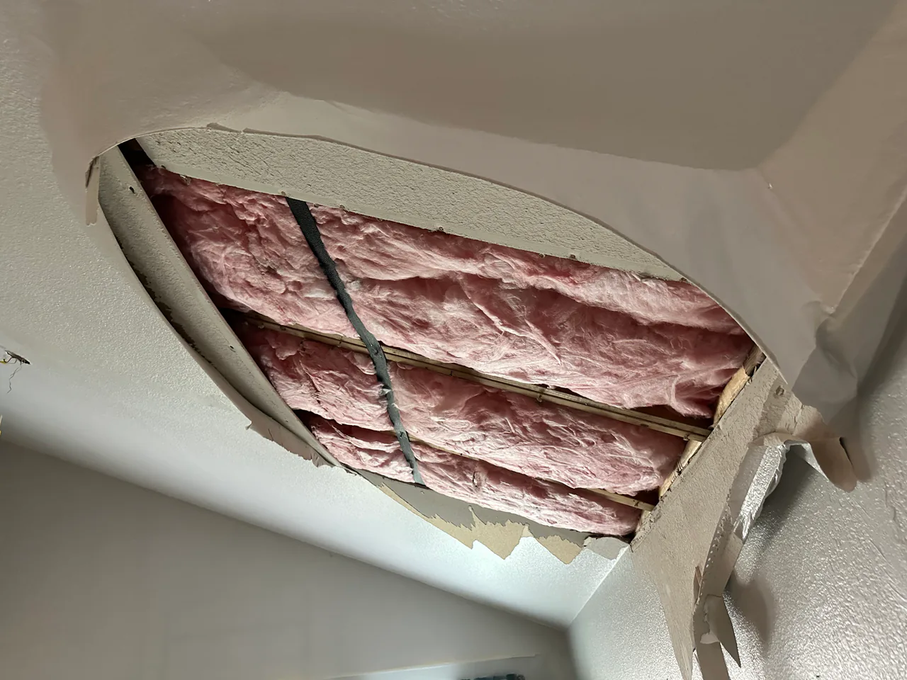 Tight ceiling flood-cut detail by Bayou City exposing pink fiberglass insulation through the opened drywall