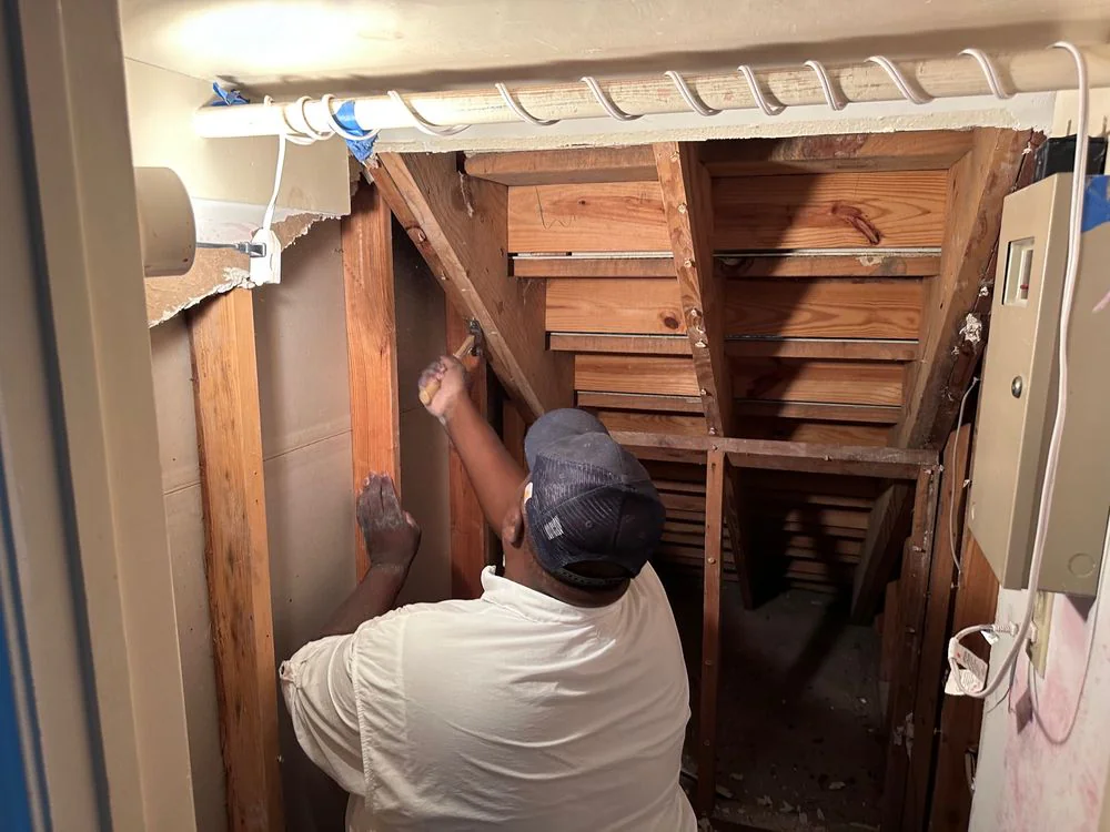 Bayou City crew member working with a hammer inside an opened wall cavity exposing wood structure during reconstruction