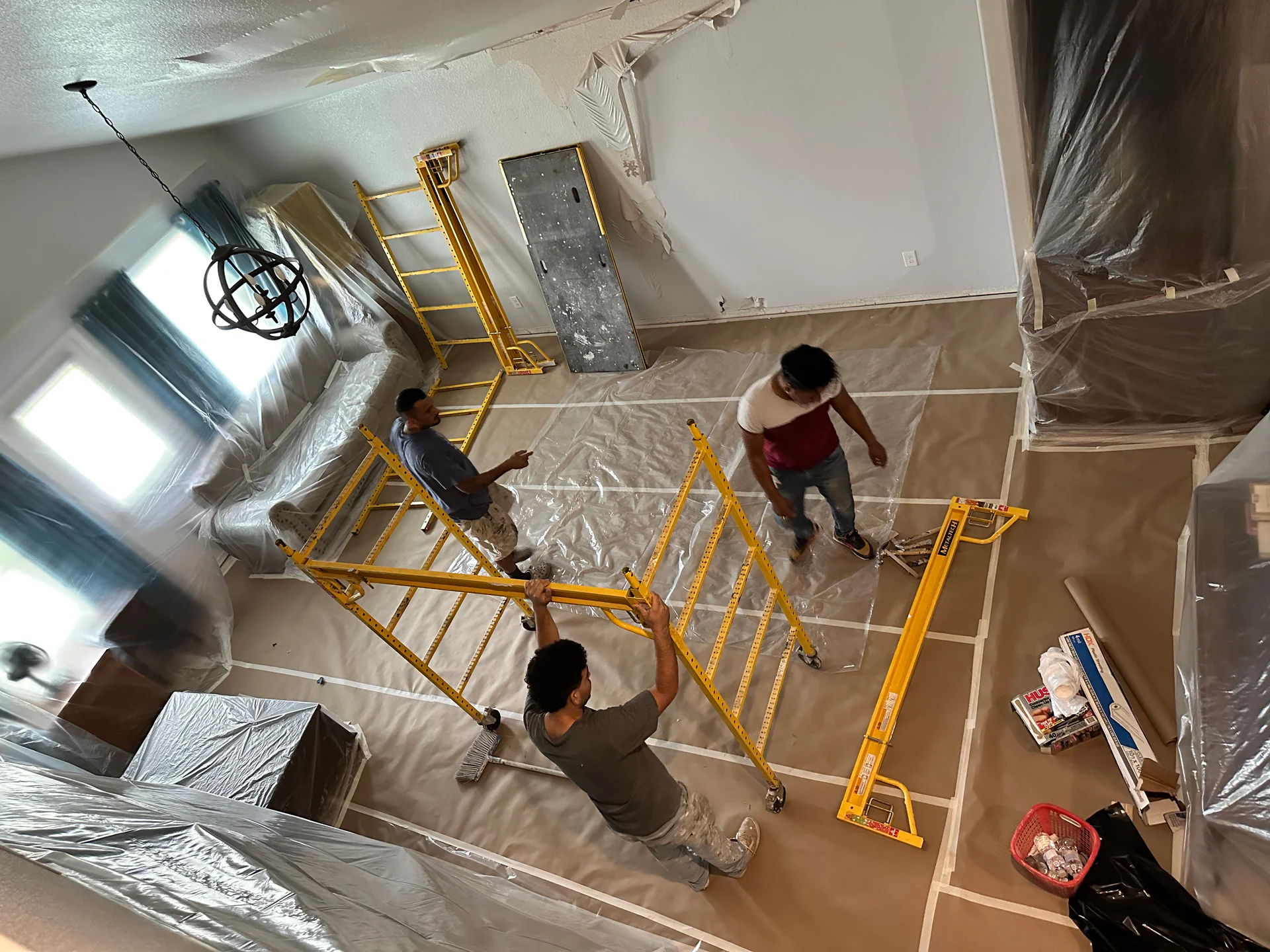 Bayou City crew assembling yellow scaffolding on plastic floor protection during an interior restoration job