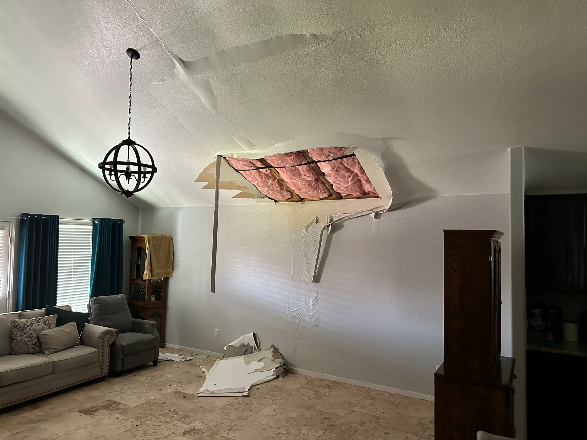 Vaulted living room ceiling with a Bayou City flood-cut exposing pink fiberglass insulation, drywall debris on the tile floor below